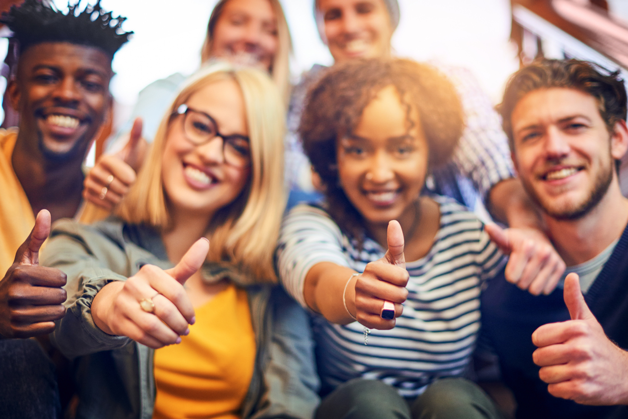 Portrait of a group of diverse university students showing a thumbs up while sitting on the staircase on campus